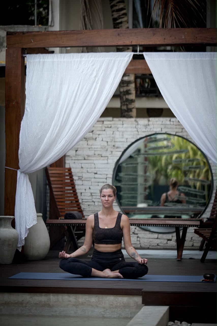 Katya Noades seated on a meditation mat in an open studio
